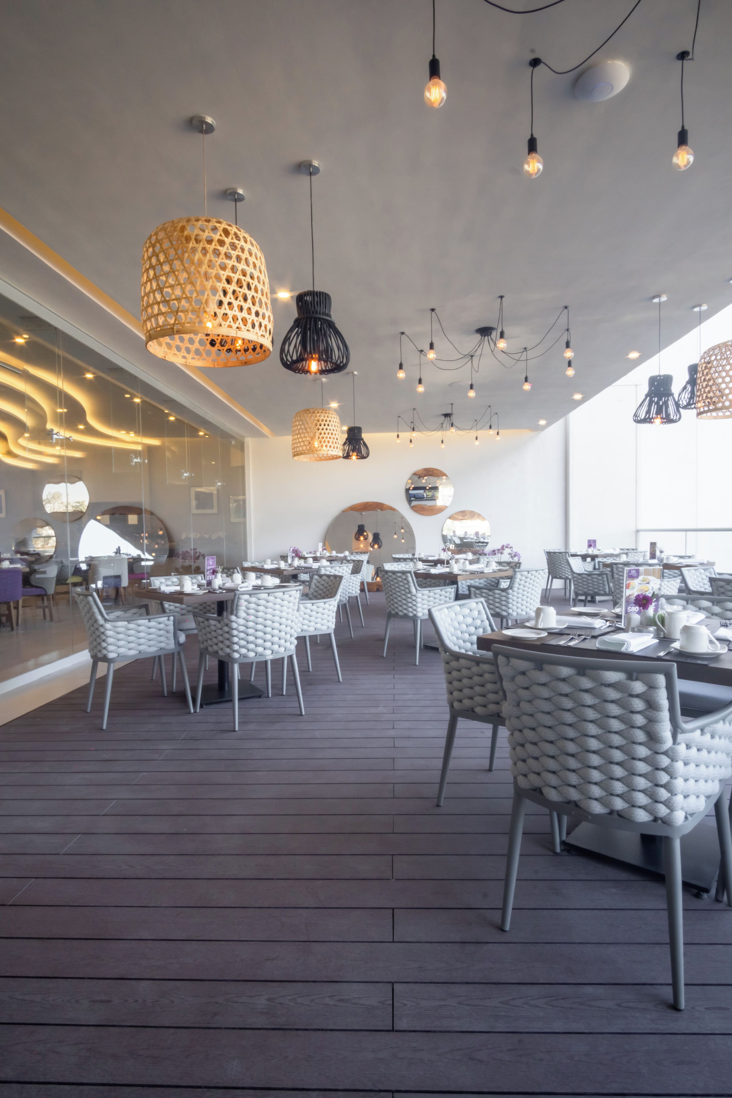 Un restaurante moderno con suelo de madera, sillas blancas acolchadas e iluminación colgante.