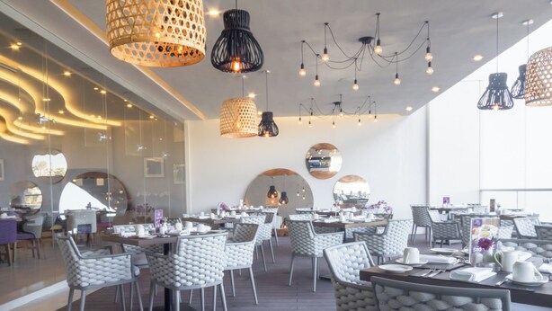 Un restaurant moderne avec un plancher en bois, des chaises blanches rembourrées et des luminaires suspendus.