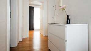 Un pasillo con piso de madera, paredes blancas, un armario blanco y un jarrón con una flor.