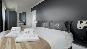 Habitación de hotel moderna con una cama grande, dos almohadas con el logotipo del hotel, una mesita de noche con una lámpara y un espejo.