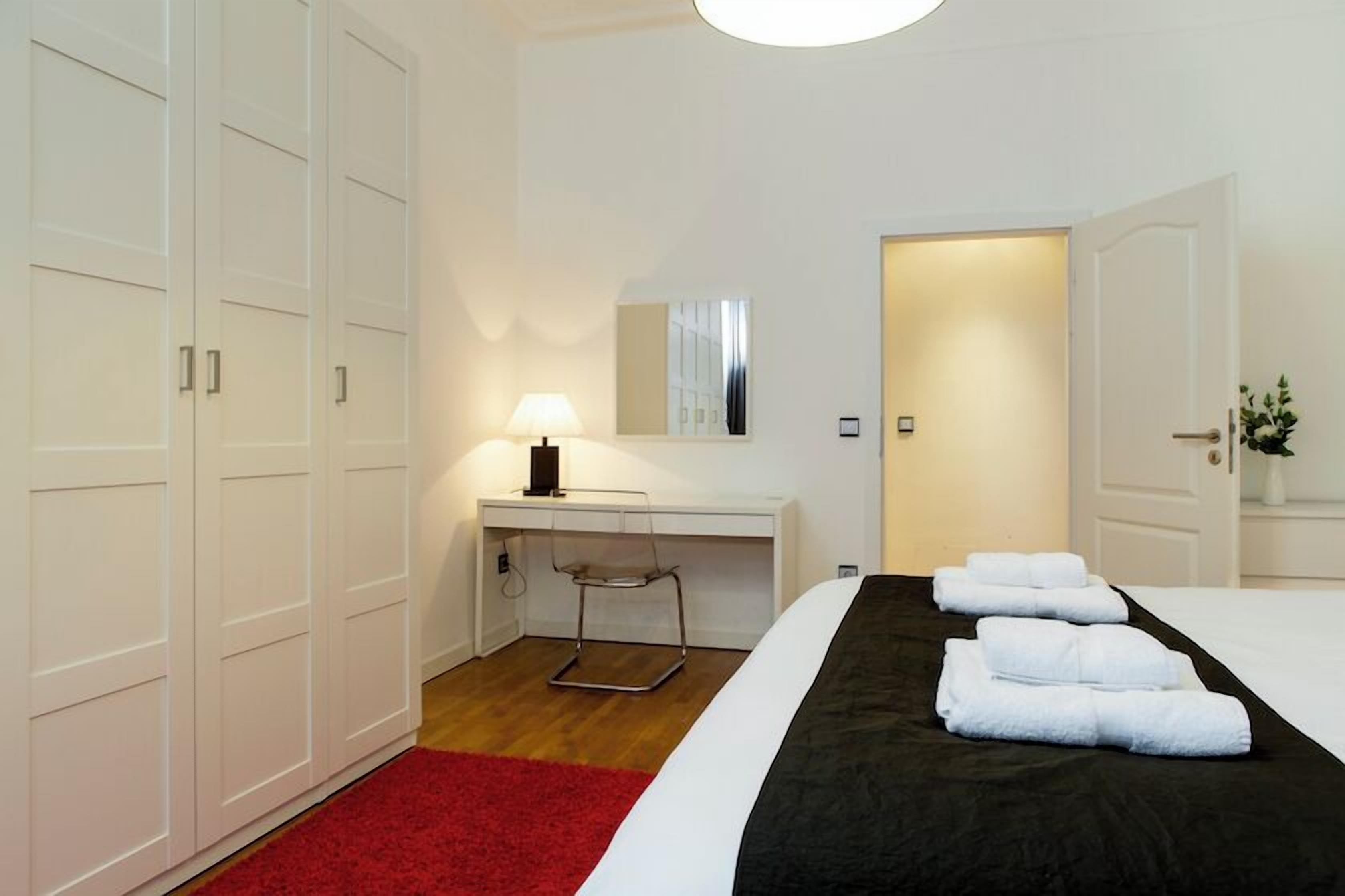 A hotel room with a bed, a desk, a chair, a lamp, and a wardrobe.