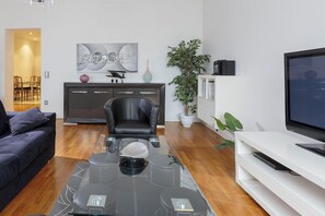 Ein modernes Wohnzimmer mit einem Glastisch, einer schwarzen Ledersofa, einer weißen Unterhaltungsecke und einem großen Flachbildfernseher.