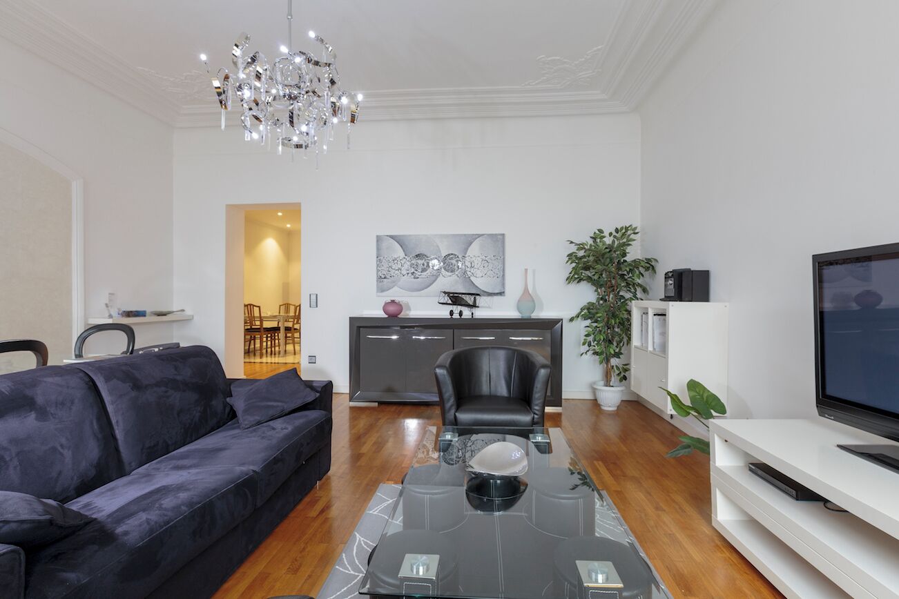 Una sala de estar moderna con un sofá, una mesa de centro de vidrio, un televisor y un comedor con sillas y un armario.