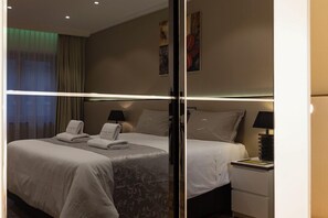 Habitación de hotel con dos camas, cada una con una almohada y una toalla, una mesita de noche con lámpara, y una pared decorada con obras de arte.