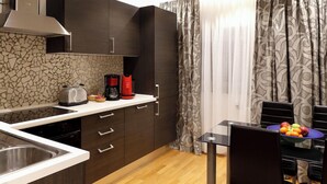 A modern kitchen with dark wooden cabinets, a white countertop, a coffee maker, and a dining area with a glass table and chairs.