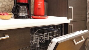 A kitchen with a dishwasher, a coffee maker, and a bowl of fruit on the counter.