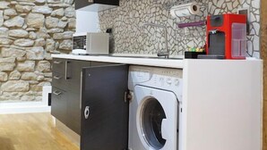 A compact kitchen with dark cabinets, a stone wall, a washing machine, and a microwave. - Liberty -52 Apartment, 1 Bedroom, Terrace (Luxembourg)