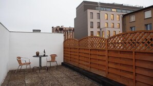 A rooftop terrace with a table and two chairs, a wooden fence, and buildings in the background. - Liberty -52 Apartment, 1 Bedroom, Terrace (Luxembourg)