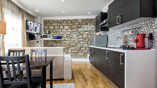 A modern kitchen with dark cabinets, a stone backsplash, and a dining area with a table and chairs. - Liberty -52 Apartment, 1 Bedroom, Terrace (Luxembourg)