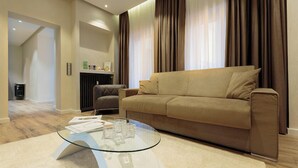 A modern living room with a beige sofa, a glass coffee table, and a fireplace. - Liberty -32 Two-Bedroom Deluxe Apartment (Luxembourg)