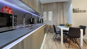 A modern kitchen with a built-in oven, microwave, and coffee maker. There is a dining area with a table and chairs, and a 'Welcome' sign on the wall. - Liberty -32 Two-Bedroom Deluxe Apartment (Luxembourg)