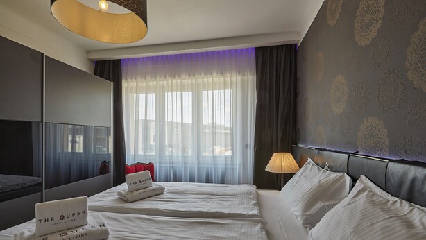 Camera d'albergo con un letto grande, una TV a schermo piatto, un comodino con una lampada e vista sulla città attraverso tende trasparenti.