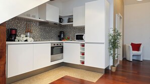 A modern kitchen with white cabinets, a stone backsplash, a built-in oven, and a microwave.