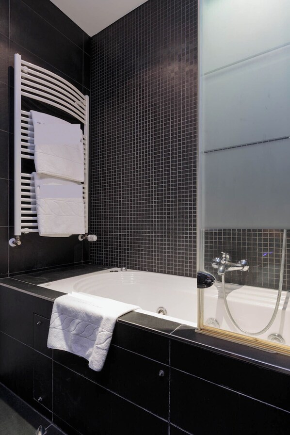 A modern bathroom with a black tiled wall, a white bathtub, and a glass-enclosed shower.
