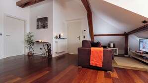 A spacious living area with a dark brown sofa, a television, and a radiator.
