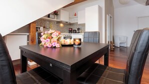 A dining area with a dark wooden table, two black leather chairs, and a vase of pink flowers.
