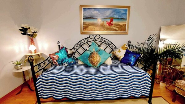 Ein Bett mit einer blau-weiß gestreiften Tagesdecke, ein Gemälde einer Strandansicht und ein roter Sessel auf dem Boden.