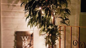 A wooden welcome sign with the text "WELCOME" next to a potted plant with hanging lights.
