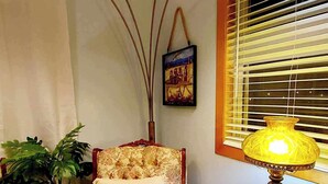 A cozy living room with a patterned armchair, a small table with a lamp, and a potted plant.