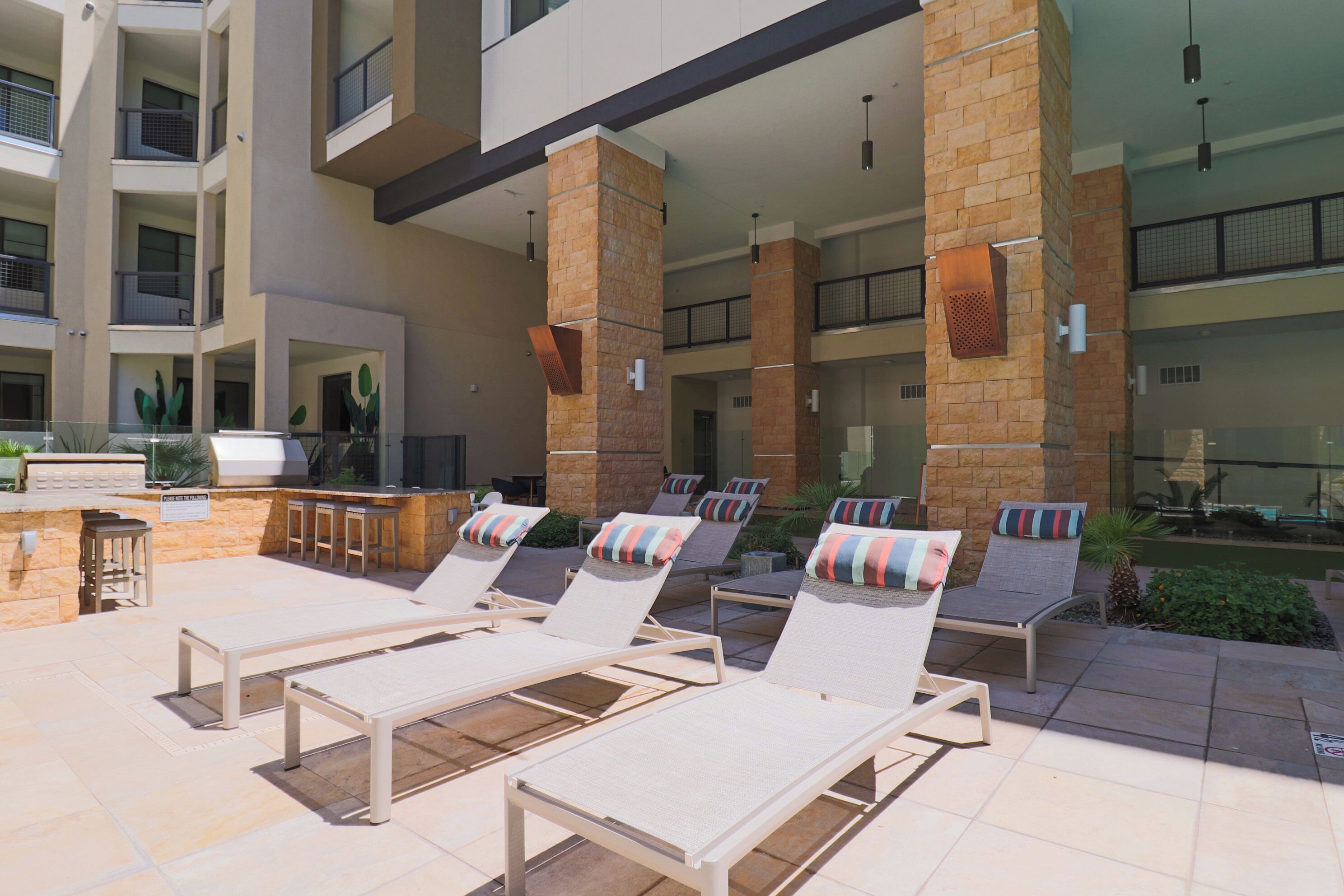 A rooftop lounge area with sun loungers, a barbecue station, and a view of the building's interior.