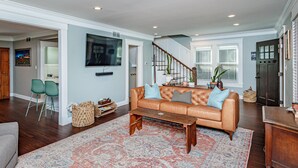 A spacious living room with a large sofa, a coffee table, and a patterned rug. There is a staircase leading to another level, and a door with a window on the right. - HOTTUB! private outdoor spaces-WALK downtown and MU. PETS OK Top Notch finishes (Columbia)