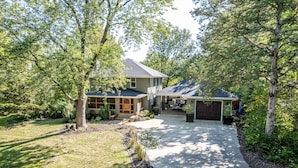 A two-story house with a covered driveway, surrounded by mature trees and a well-maintained lawn. - HOTTUB! private outdoor spaces-WALK downtown and MU. PETS OK Top Notch finishes (Columbia)
