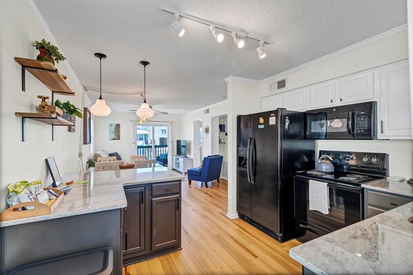 A modern kitchen with dark cabinetry, a central island, and a dining area with a blue chair.