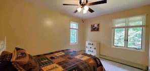 Ein Schlafzimmer mit Bett, Schminktisch, zwei Fenstern und Deckenventilator.