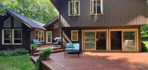 A modern house with a deck, two blue chairs, and a wooden staircase.