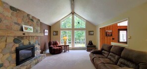 A cozy living room with a stone fireplace, a large window, and a comfortable couch. - Fairway House Close to Crystal Lake Golf (Beulah)