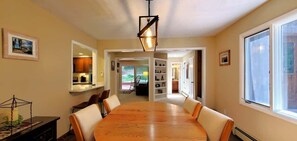 A dining area with a large wooden table, white chairs, and a hanging light fixture.