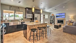 A modern kitchen with a central island, bar stools, a built-in microwave, and a large TV in the living area. - Scottsdale Retreat Outdoor Oasis w/Heated Pool & Spa, Outdoor Kitchen & 100" TV (Scottsdale)