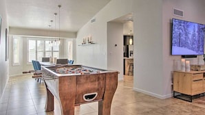 A spacious living area with a foosball table, a television mounted on the wall, and a kitchen in the background. - Scottsdale Retreat Outdoor Oasis w/Heated Pool & Spa, Outdoor Kitchen & 100" TV (Scottsdale)