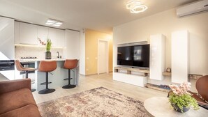 A modern living room with a flat-screen TV, a coffee table, and a bar area with stools.