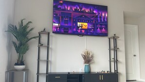 A living room with a flat-screen TV mounted on the wall, a dark-colored entertainment unit, a potted plant, and a decorative vase. - New house! Special promo for 1+ week rental, 5% off, 1+ month rental 11% off! (Cape Coral)