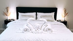 A neatly made bed with white linens and towels arranged in a heart shape. There is a painting on the wall above the bed, and two bedside tables with lamps and decorative items. - New house! Special promo for 1+ week rental, 5% off, 1+ month rental 11% off! (Cape Coral)