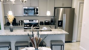 A modern kitchen with stainless steel appliances, a central island, and pendant lighting. - New house! Special promo for 1+ week rental, 5% off, 1+ month rental 11% off! (Cape Coral)