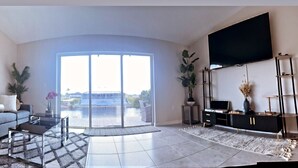 A spacious living room with a large sliding glass door leading to a balcony, a flat-screen TV mounted on the wall, and a modern entertainment unit. - New house! Special promo for 1+ week rental, 5% off, 1+ month rental 11% off! (Cape Coral)