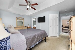 A bedroom with a bed, a ceiling fan, a TV, a dresser, and a door. - Greenway Getaway 3BR Cottage (Myrtle Beach)