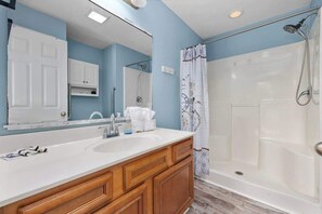 A bathroom with a sink, mirror, cabinets, shower, and a door. - Greenway Getaway 3BR Cottage (Myrtle Beach)