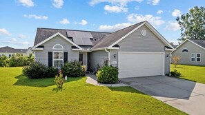 A residential house with a garage, solar panels, and a well-maintained lawn. - Greenway Getaway 3BR Cottage (Myrtle Beach)
