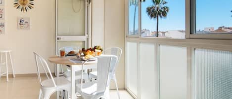 A dining area with a table set for two, white chairs, and a breakfast spread.