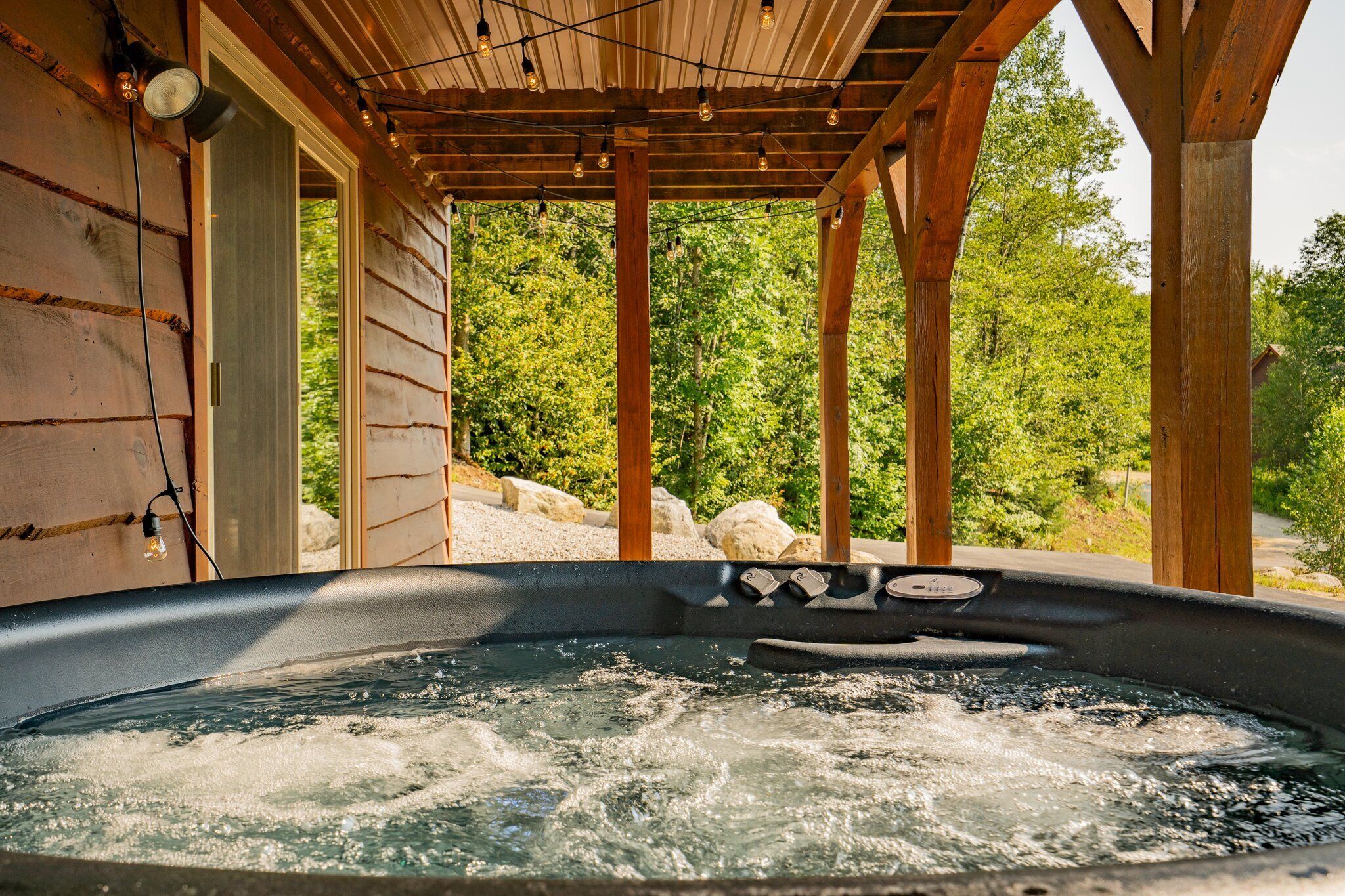A hot tub under a wooden pergola with a view of trees and rocks.