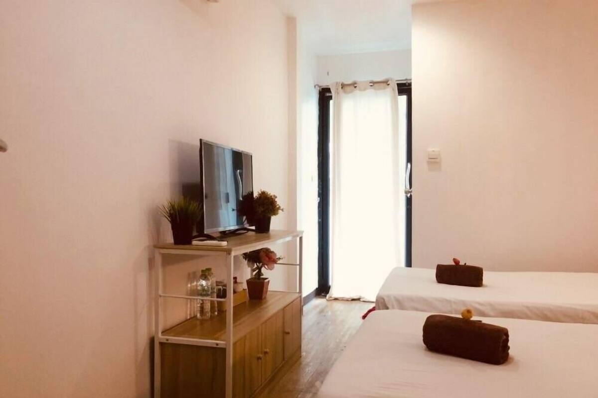 A hotel room with a TV on a shelf, two beds with pillows, a wooden cabinet, and a door leading outside.