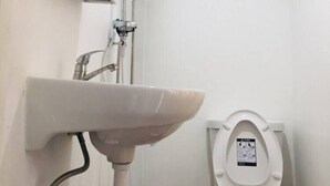 A bathroom with a pedestal sink, a toilet, and a shower. - Owl's Nest Hostel (Bangkok)