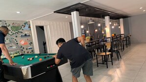 A pool table in a room with a dining area and a mural on the wall. - Owl's Nest Hostel (Bangkok)