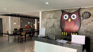 A hotel reception area with a modern design, featuring a large wall mural of an owl, a reception desk, and a seating area with tables and chairs. - Owl's Nest Hostel (Bangkok)