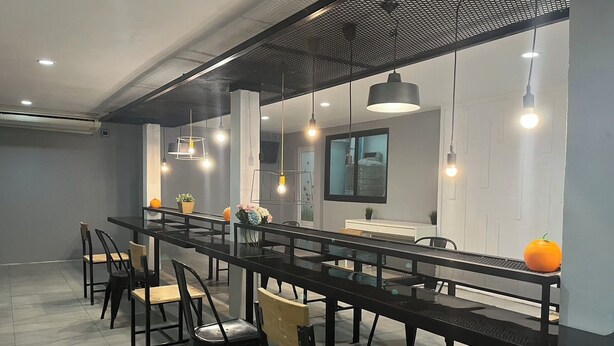 A modern dining area with a long black table, black chairs, and pendant lighting. - Owl's Nest Hostel (Bangkok)