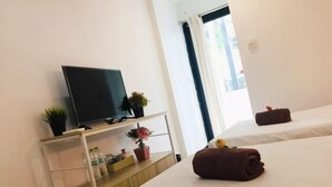 A hotel room with a bed, a TV on a shelf, a window, and a small table with toiletries. - Owl's Nest Hostel (Bangkok)