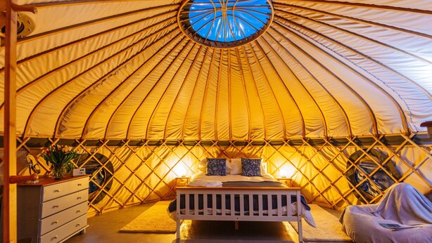 Ein gemütliches Zeltinneres mit einem Bett, einer Kommode und einem kleinen Tisch mit Lampe.